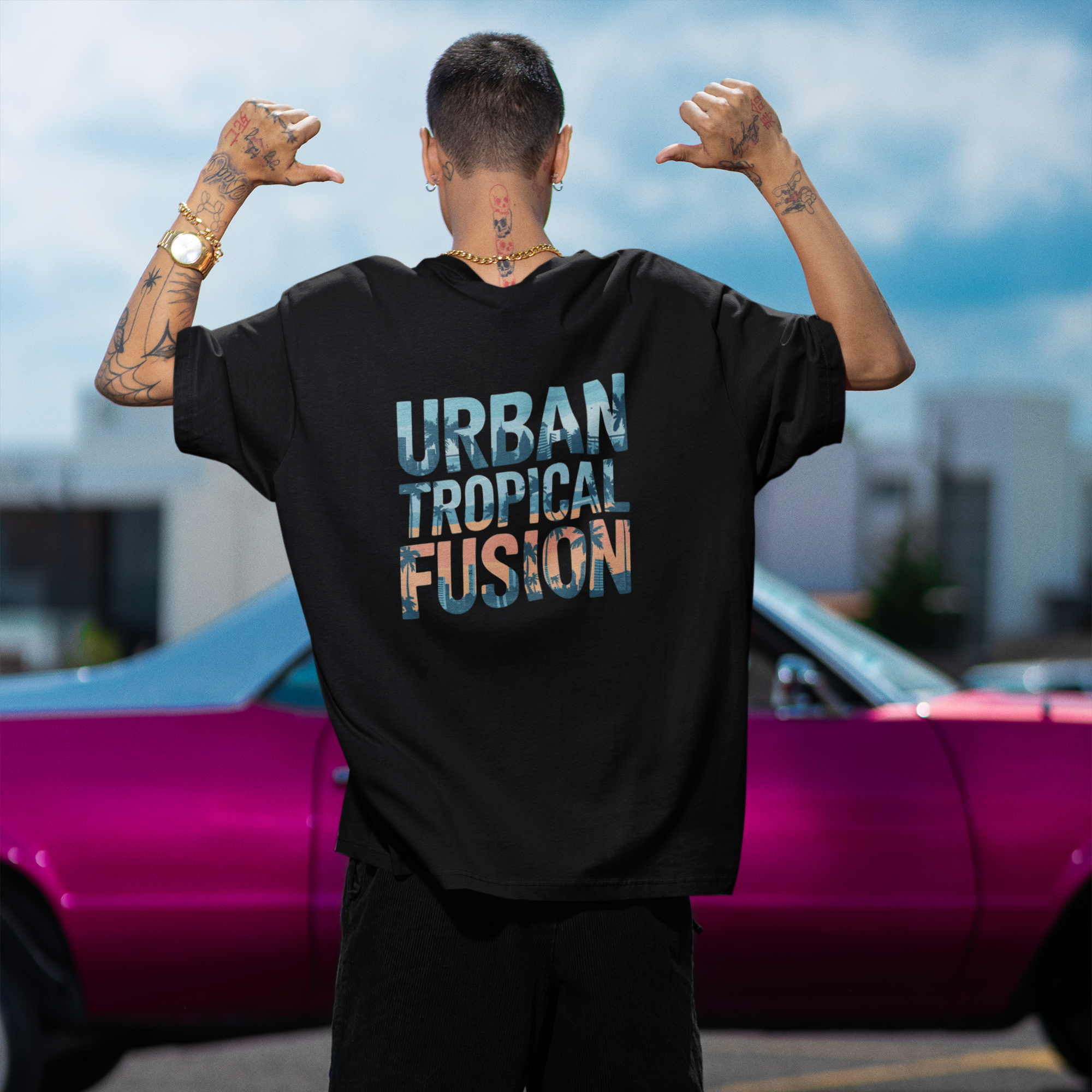 Person wearing a black t-shirt with 'Urban Tropical Fusion' text, standing in front of a pink car.