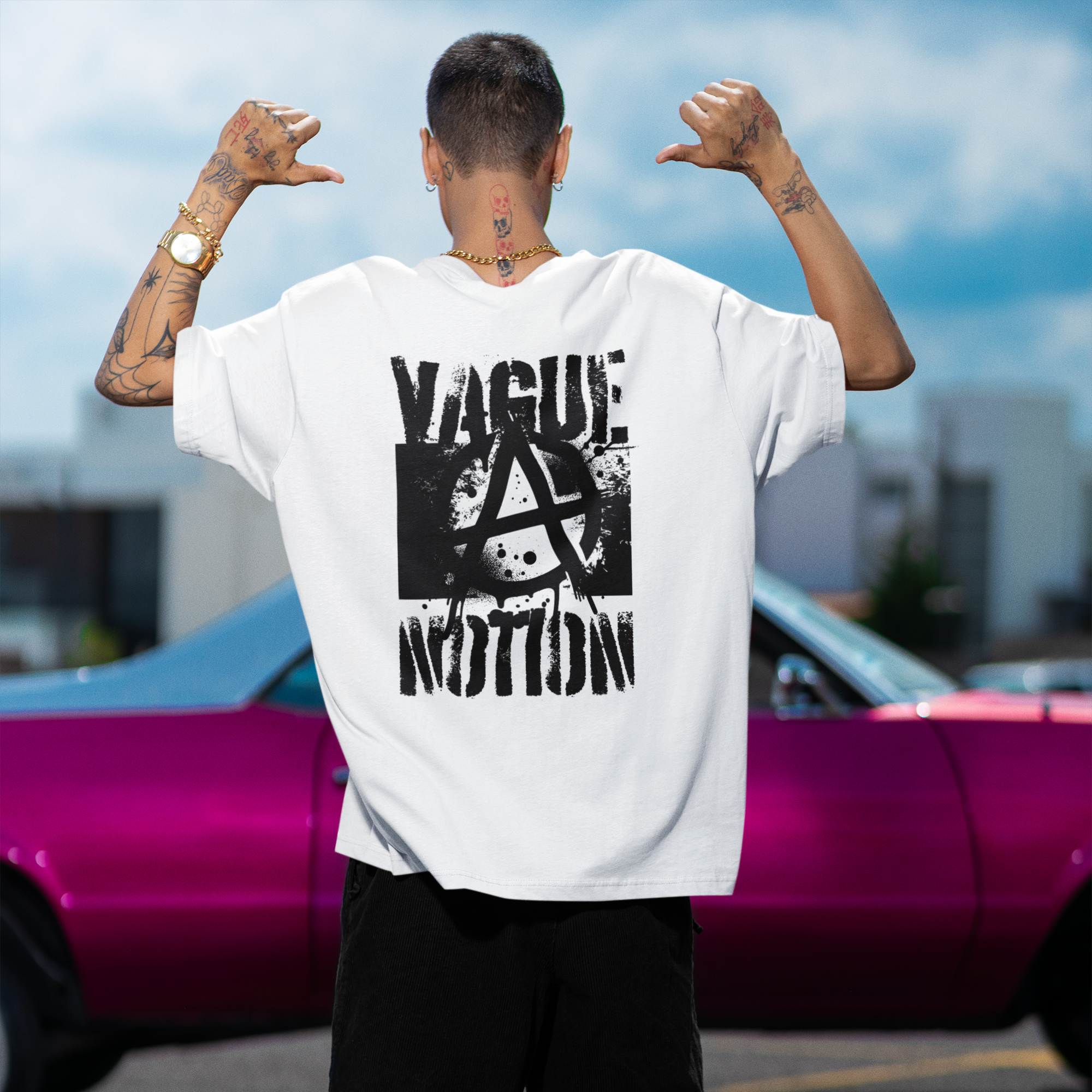 Person wearing a white t-shirt with black text and graphics, standing in front of a pink car.