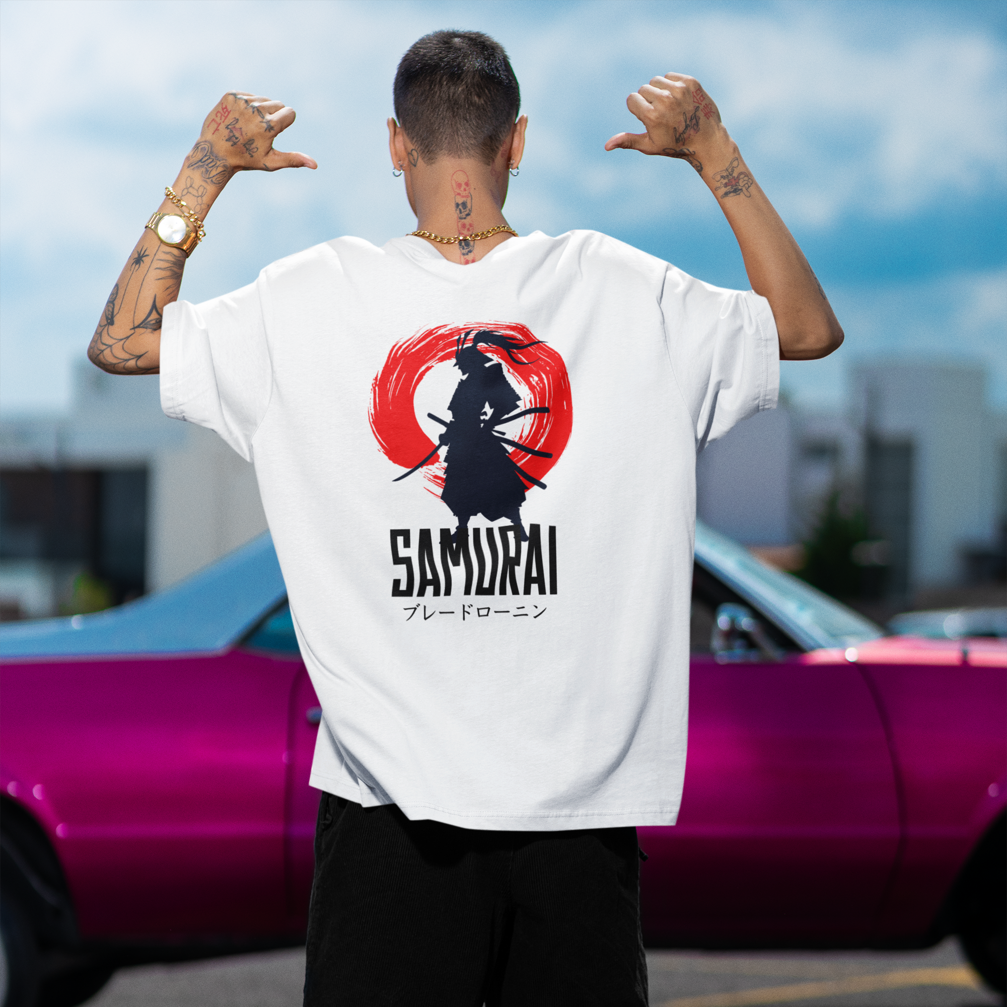 Person wearing a white t-shirt with a Samurai design and text, standing in front of a pink car.