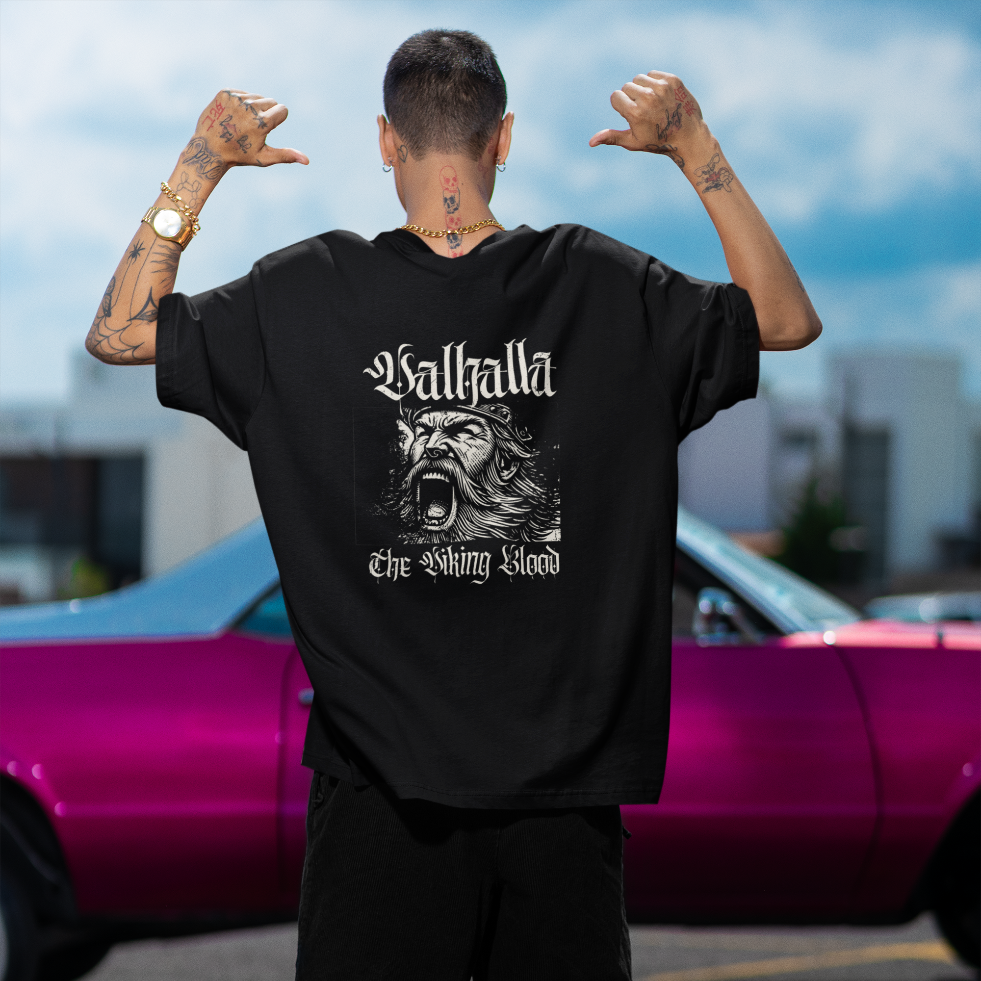 Person wearing a black t-shirt with 'Baltha' design and text, standing in front of a pink car.