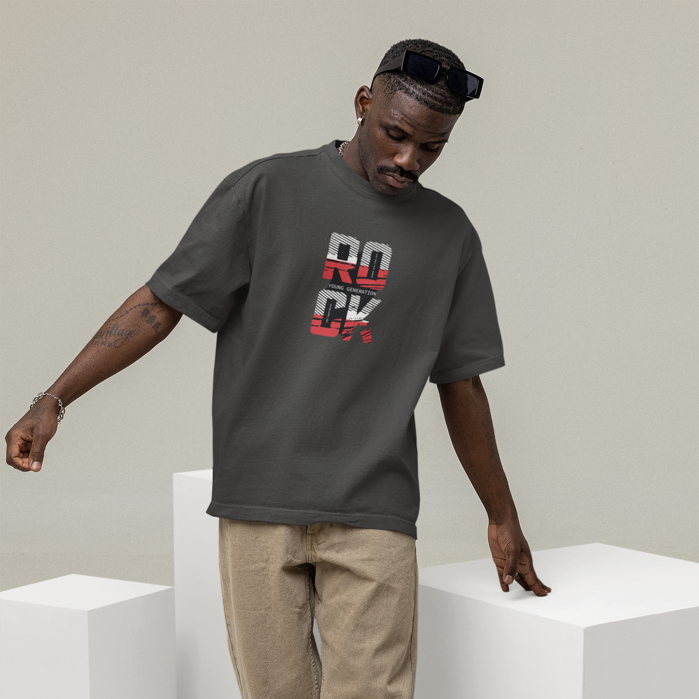 Man wearing a gray t-shirt with 'ROCK' print, beige pants, and white sneakers on a light background