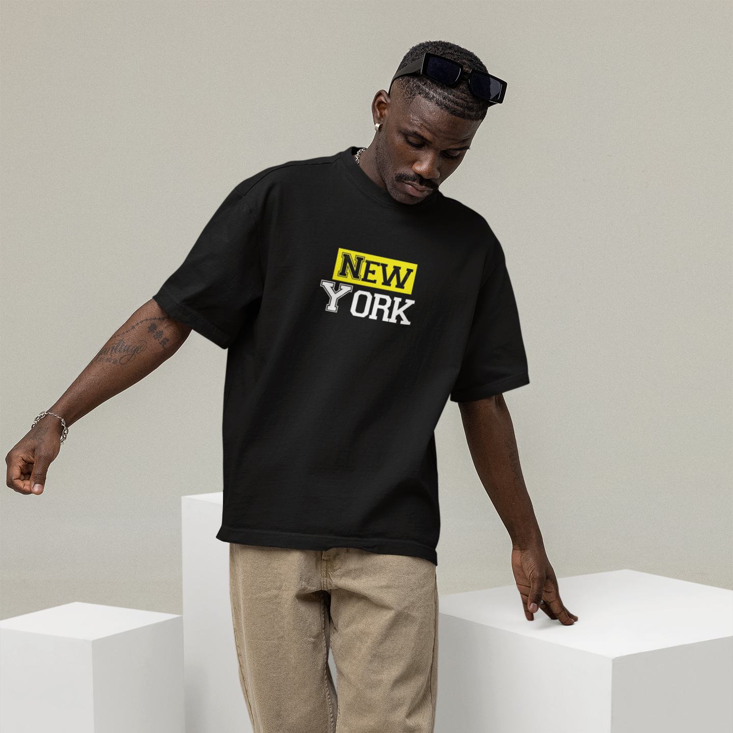 Man wearing a black t-shirt with 'New York' text, standing on white cubes against a plain background