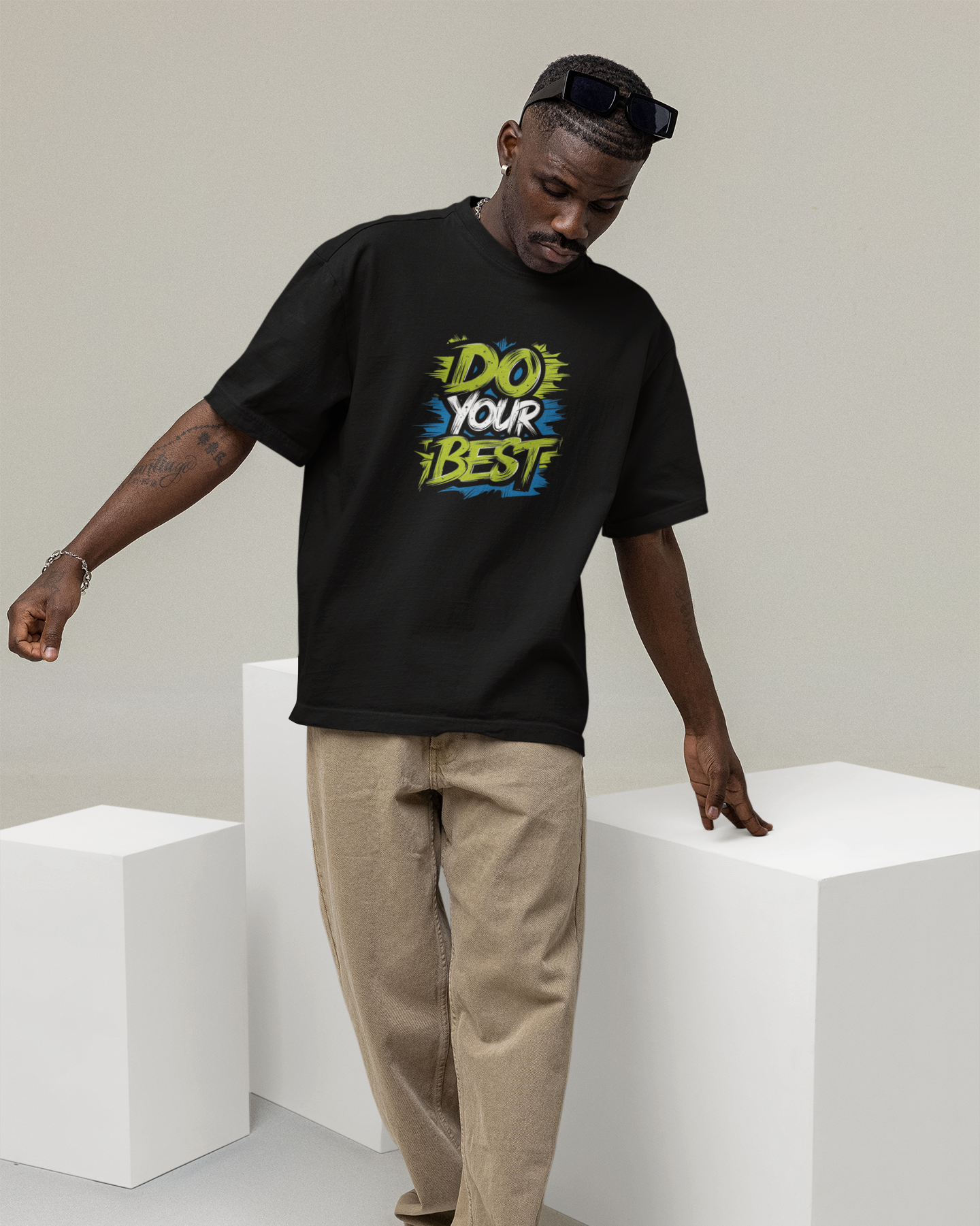 Man wearing a black t-shirt with colorful text design, standing on white cubes against a plain background