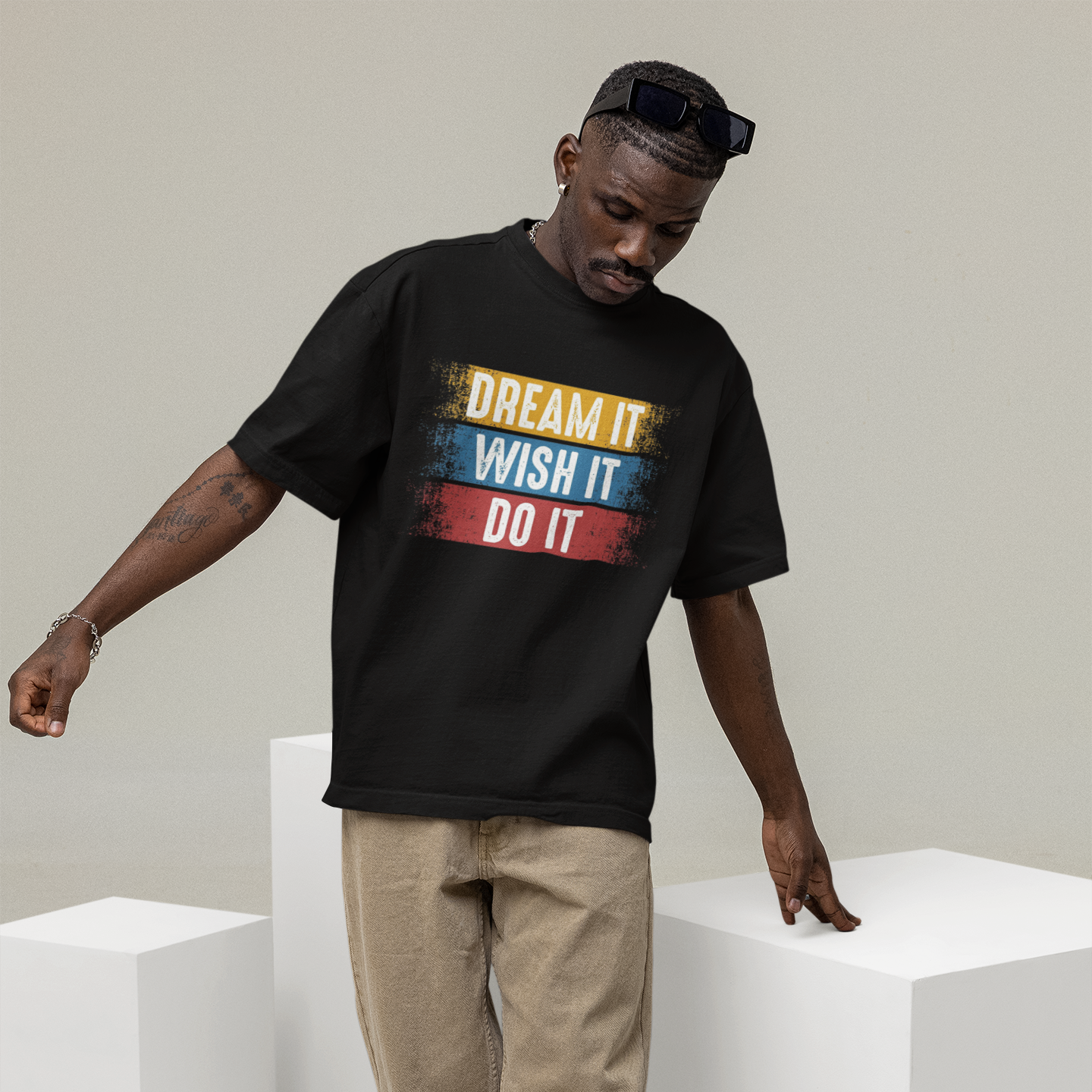 Man wearing a black t-shirt with colorful text design, standing on white cubes against a plain background