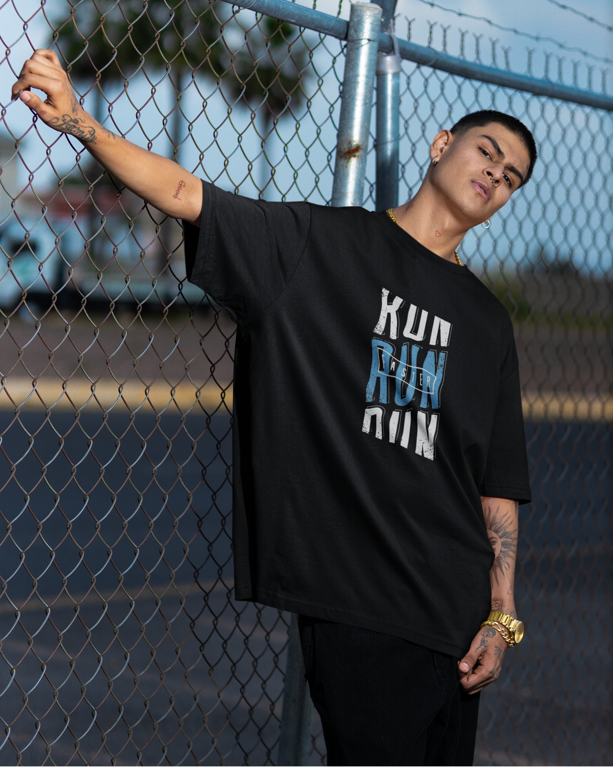 Person wearing a black t-shirt with text, standing against a chain-link fence.
